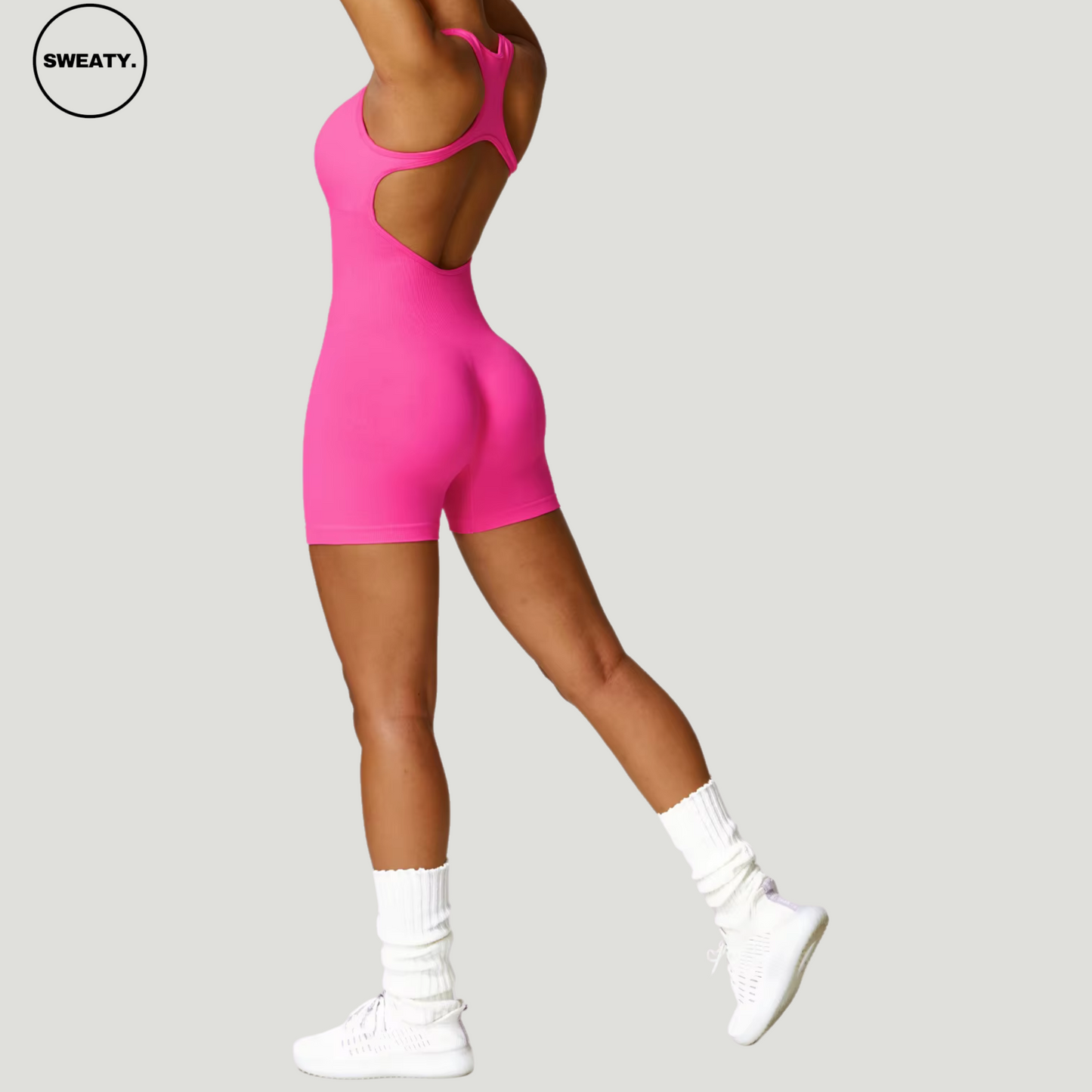 Hot pink seamless gym shortie jumpsuit by SWEATY - Women's side view showcasing the flattering, figure-enhancing fit. The open-back racerback design allows for greater mobility, perfect for fitness and active wear.