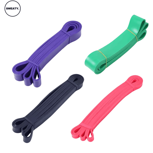 Set of four fitness resistance bands in purple, green, black, and pink colors, displayed from a top angle. Durable and versatile bands ideal for strength training, stretching, and resistance exercises. SWEATY fitness equipment for effective home and gym workouts.