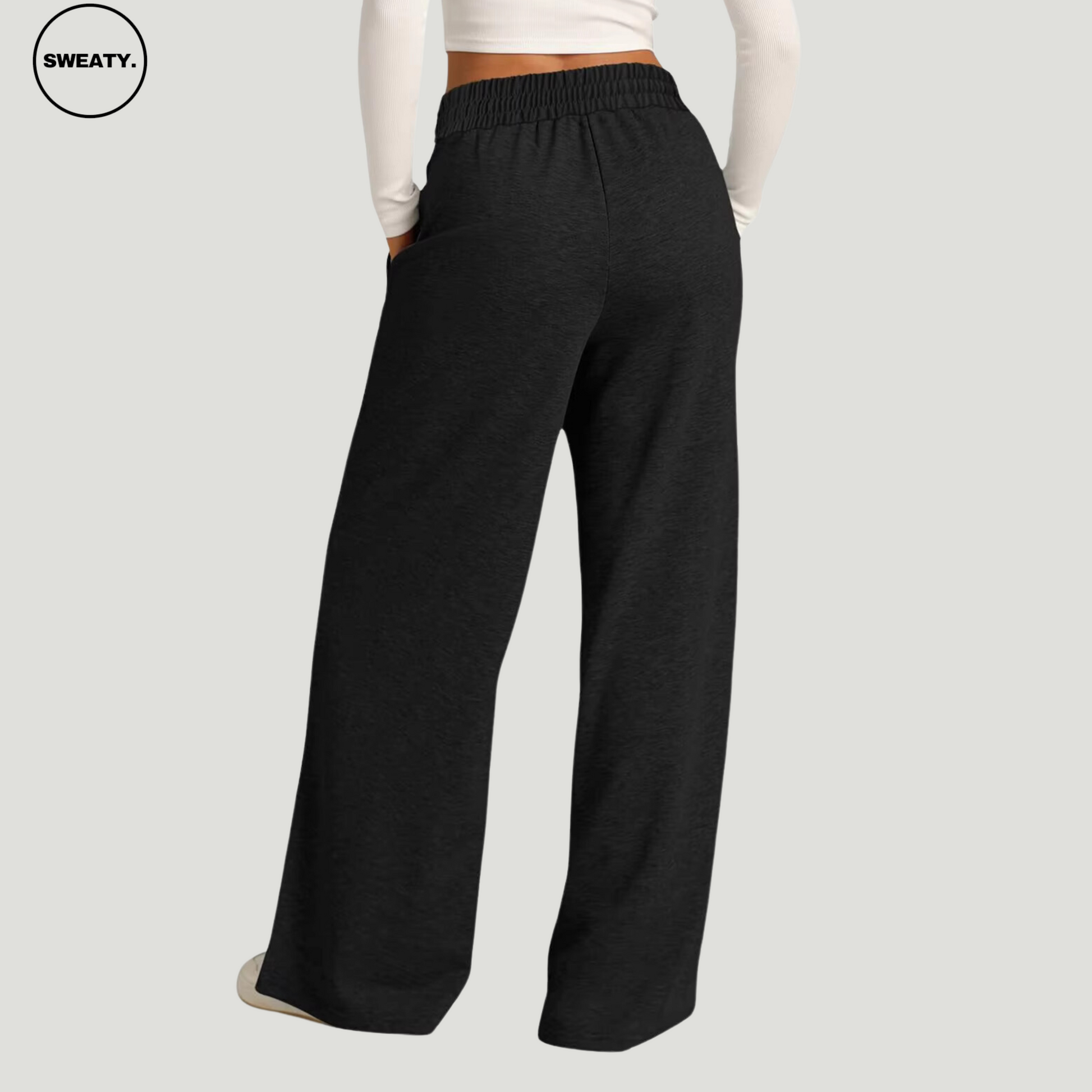 Back view of a woman wearing black wide-leg fleece-lined sweatpants, featuring an elastic waistband and a relaxed fit, paired with a white long-sleeve crop top. The comfortable sweatpants have side pockets and a loose, casual design.