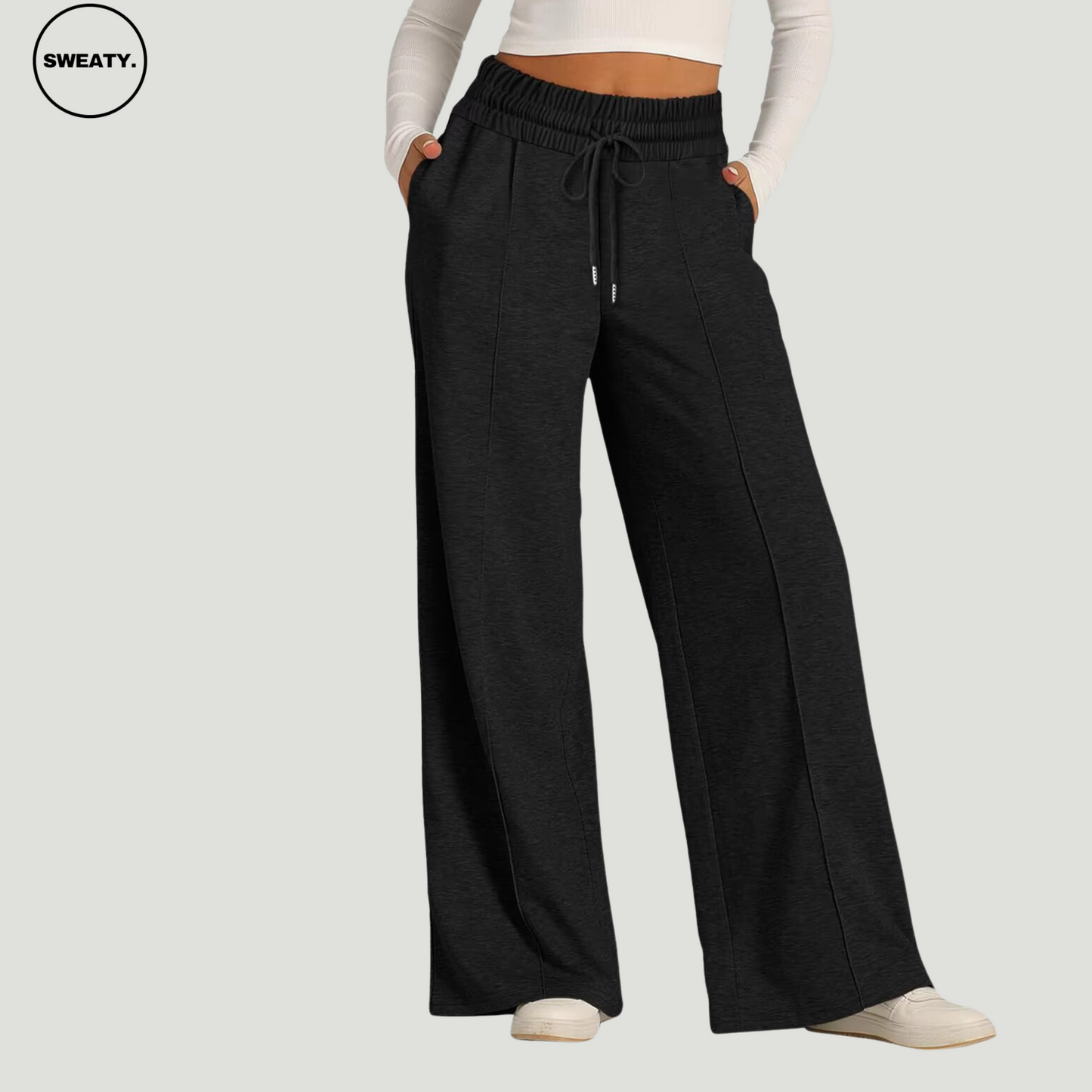 Front view of a woman wearing black wide-leg fleece-lined sweatpants with an elastic waistband and drawstring, paired with a white long-sleeve crop top, showcasing a relaxed and comfortable fit for casual wear.