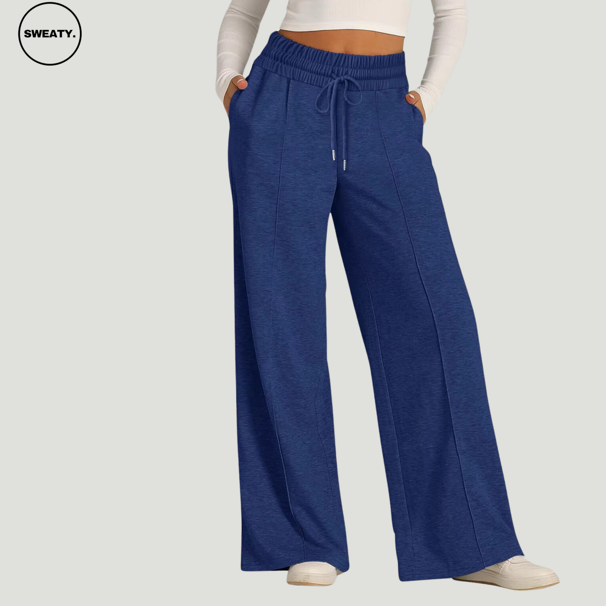 Front view of a woman wearing dark blue wide-leg fleece-lined sweatpants, featuring an elastic drawstring waistband and side pockets. The sweatpants offer a relaxed, loose fit, ideal for casual wear or lounging. Paired with a white long-sleeve crop top and white sneakers.