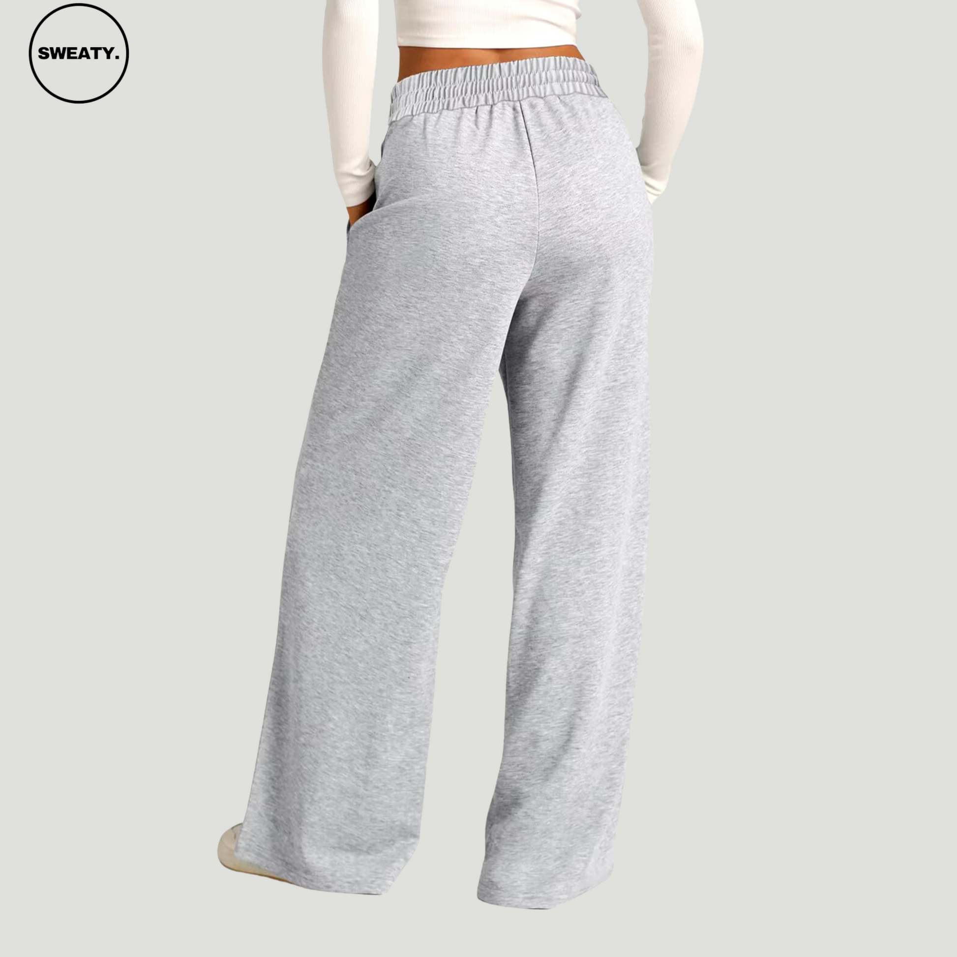 Back view of a woman wearing light grey wide-leg fleece-lined sweatpants with an elastic waistband and side pockets. The relaxed-fit pants offer a comfortable and casual style, ideal for lounging or everyday activities. Paired with a white long-sleeve crop top and white sneakers.