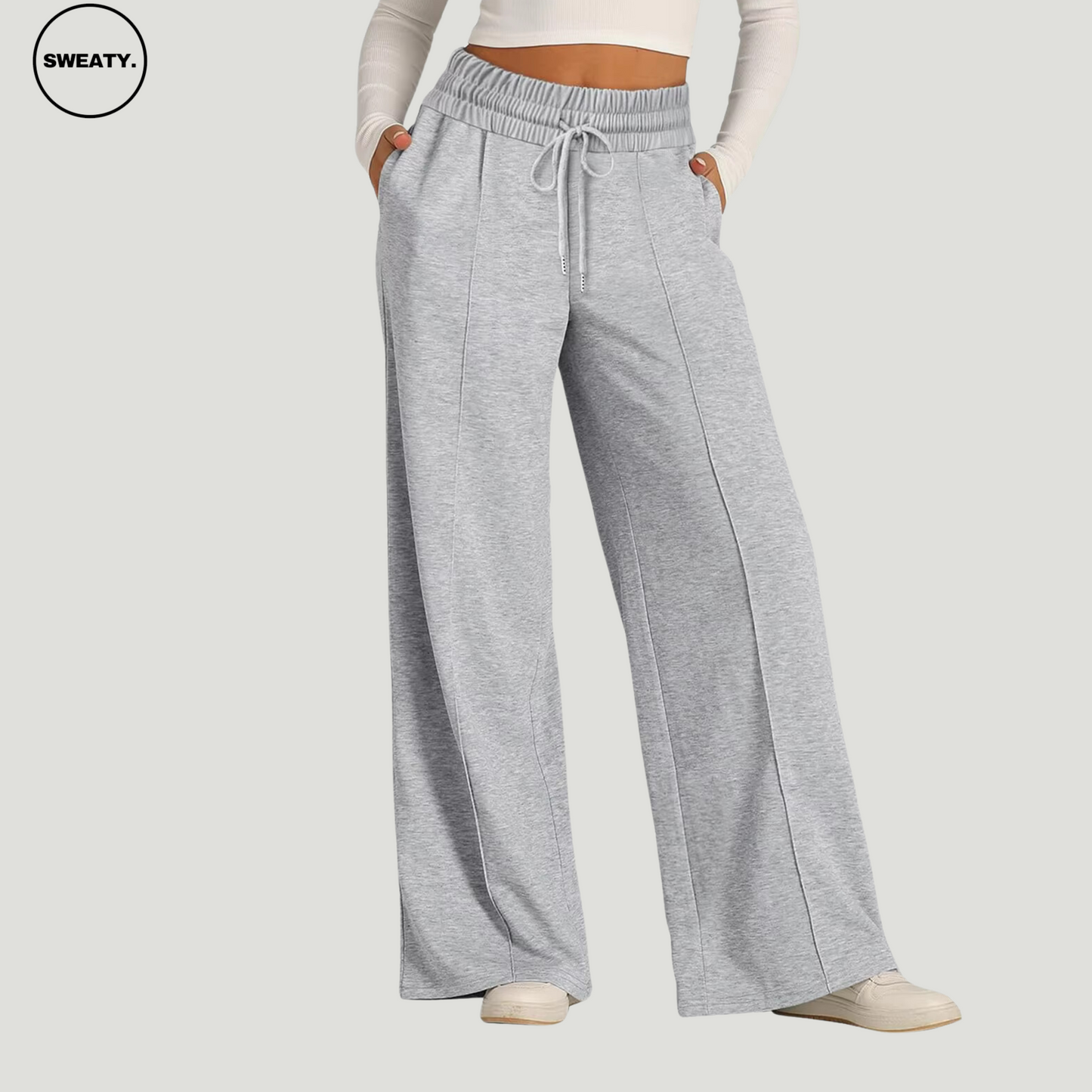 Front view of a woman wearing light grey wide-leg fleece-lined sweatpants with an elastic drawstring waistband and side pockets. The relaxed-fit pants are paired with a white long-sleeve crop top and white sneakers, offering a casual and cozy style for lounging or daily wear.